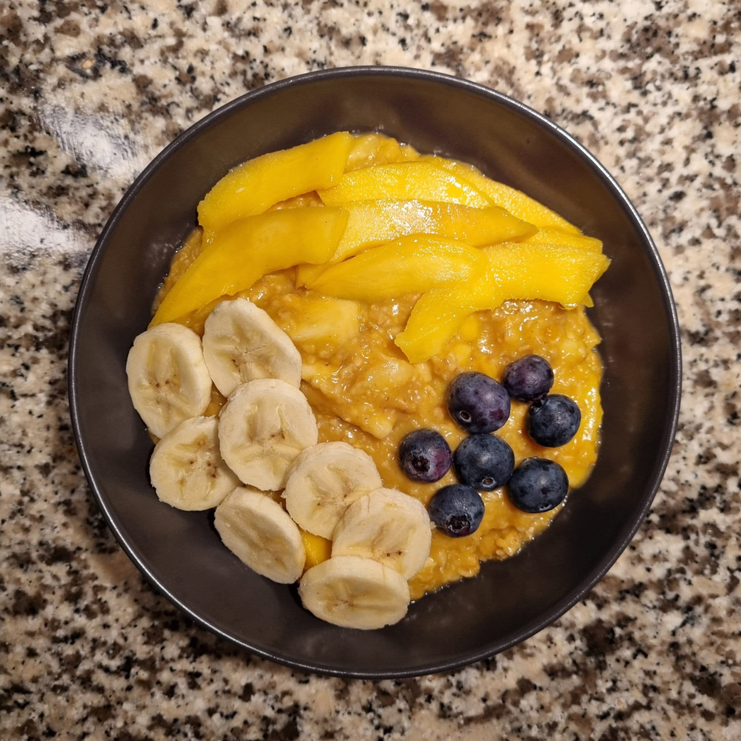 Gelbes Porridge mit Mango, Banane und Blaubeeren Rezeptbild