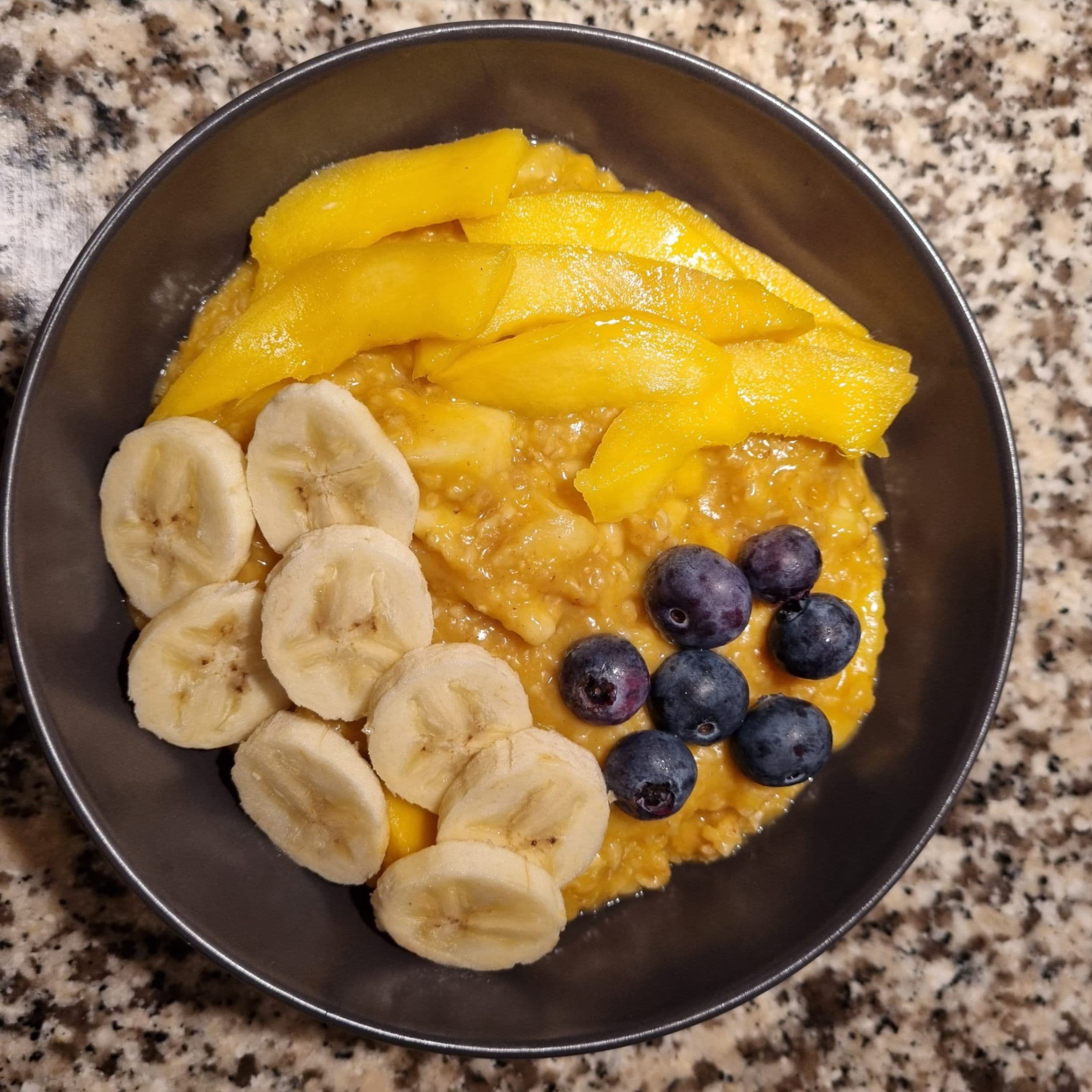 Gelbes Porridge mit Mango, Banane und Blaubeeren Rezeptbild