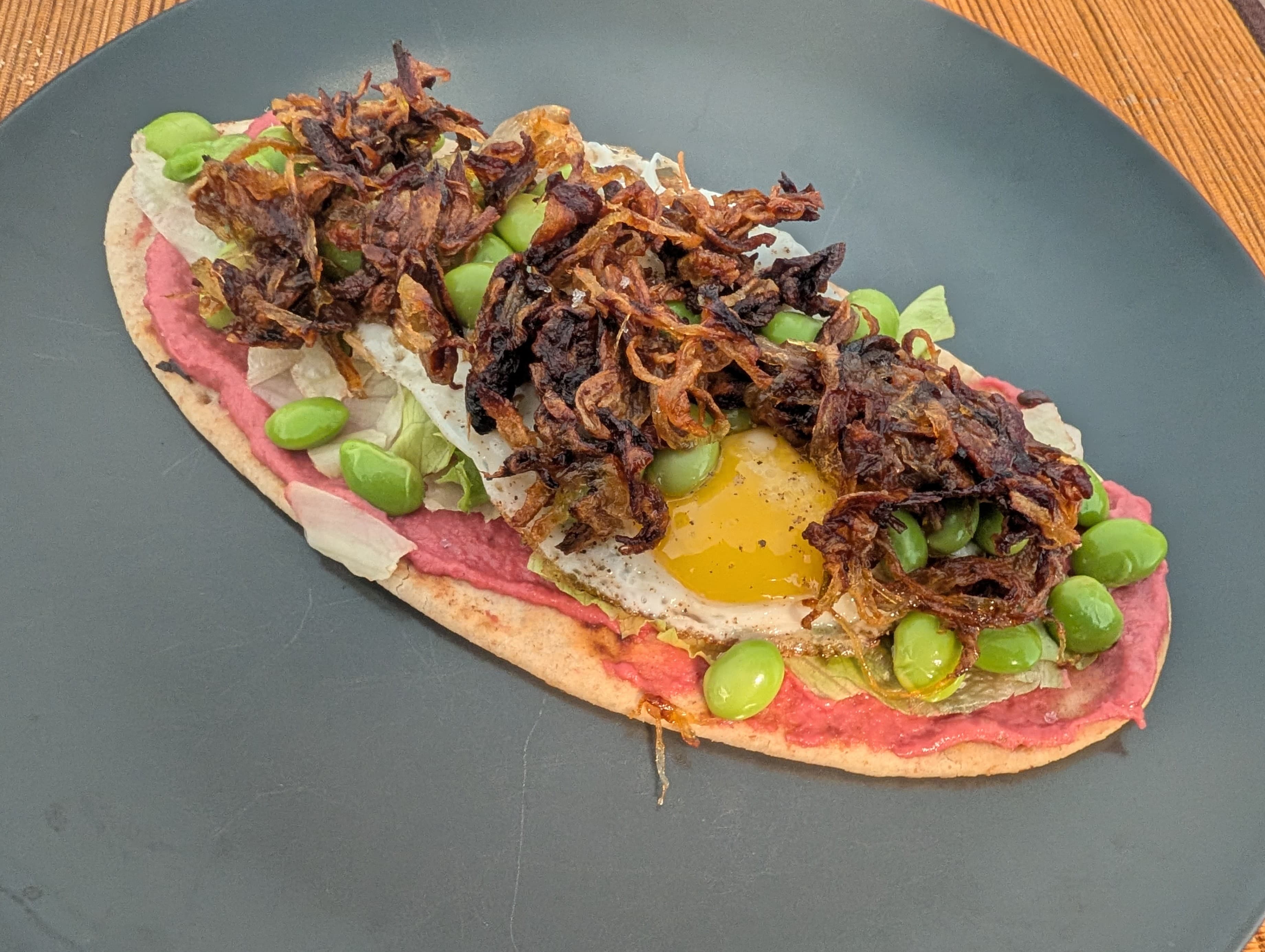 Плосък хляб с хумус от червено цвекло, пържено яйце, едамаме и карамелизиран лук Recipe Image